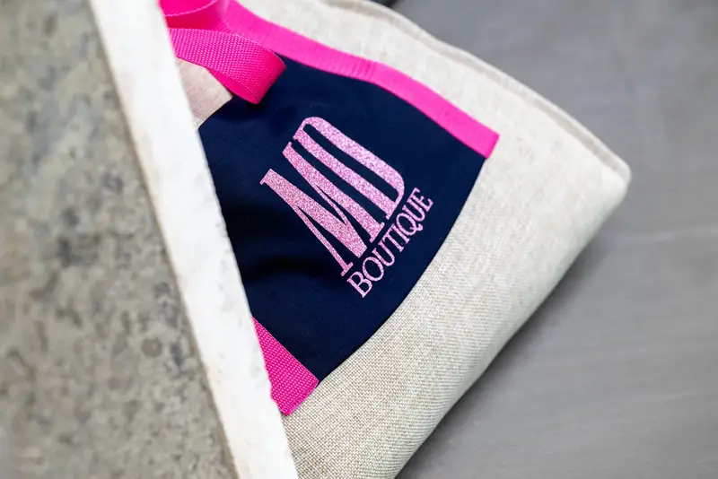 Dettaglio fucsia e blu del logo MD Boutique su una pochette in tessuto